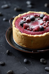 Healthy Scandinavian dessert. Open lingonberry pie with raw raspberries and currants on black background copy space