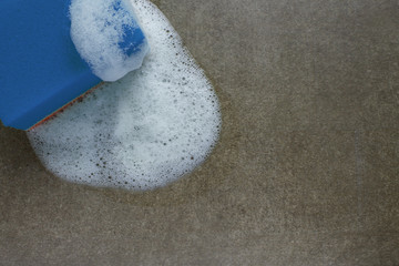 Obraz premium Cleaning green sponge with white foam on a gray-brown surface close-up with copy space. Concept-clean