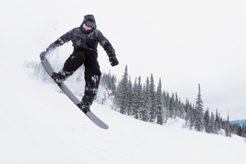 Amateur snowboarder is jumping from small kicker in the winter forest.