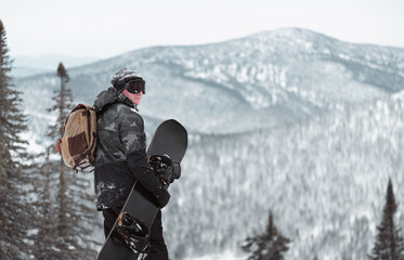 Snowboarder with snowboard in the winter forest in the mountains.