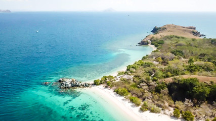 Fototapeta na wymiar A drone shot of a paradise island with some boats anchored around in Komodo National Park, Flores, Indonesia. Green middle part of the island turns into white sand beach and further into turquoise sea
