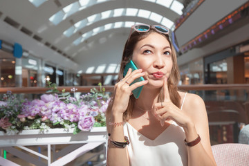 Fototapeta premium Asian woman with funny face expression talking by phone in cafe