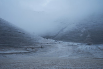 Mountain pass covered by low clouds in a snow storm