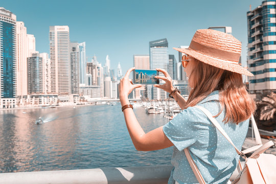 Happy Asian tourist girl taking photos in popular Marina district in Dubai for her social media and blog
