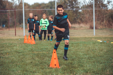 Young player in soccer jersey running between cones and ring ladder marker