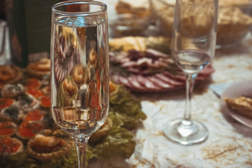 A glass of sparkling champagne on the background of a festive table. A couple of glasses of sparkling wine on a background of salads and shrimp tartlets.
