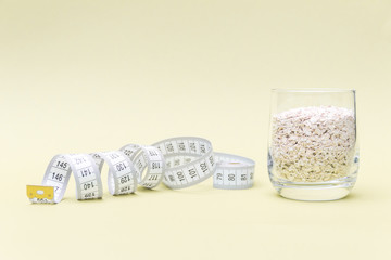 Measuring meter and glass of oat flakes on yellow background. Diet concept.