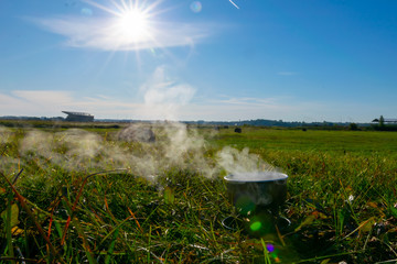 Camping stove and steam coming out of the bowl in a sunny spring day  with blue sky during camping adventure. Lithuania countryside.