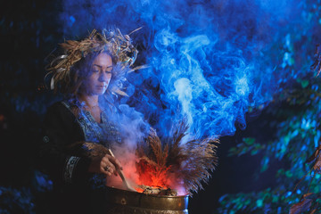 A forest witch brews a potion holding a Voodoo doll.