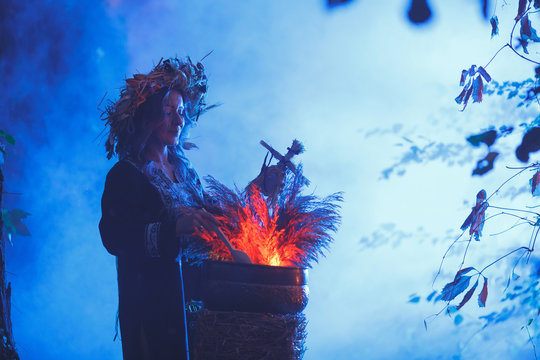 A forest witch brews a potion holding a Voodoo doll.