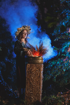 A forest witch brews a potion holding a Voodoo doll.