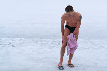 A man is rubbed with a towel while standing in the cold after swimming in the cold water in winter