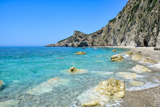 Paleokastritsa / Corfu, Greece - Chomi beach (Paradise), white-yellow-brown rocks in layers, a white pebble beach near the transparent turquoise Ionian Sea, in the summer afternoon
