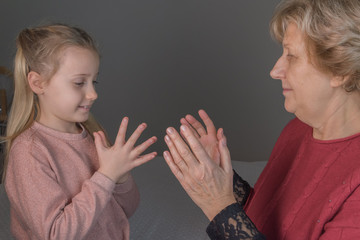 Smiling granddaughter and grandmother playing clapping games on sofa in living room at home. Girl teach to play in clapping games. Side view.