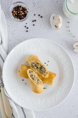 Traditional Russian thin pancakes or crepes stuffed with mushrooms with onion, garlic, herbs, cheese and cream on a white plate with sour cream. top view, vertical