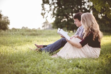 Couple reading the bible together in a garden under sunlight with a blurry background