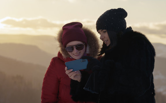 Two girls in winter wear looking at pictures on blue smartphone.