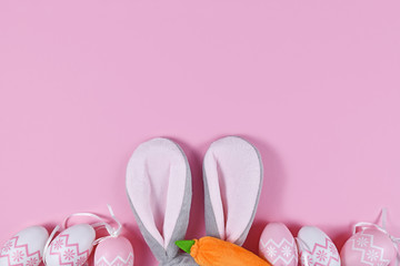 Cute Easter flat lay with plush bunny ears costume headband and easter eggs at bottom and empty copy space at top on pink background