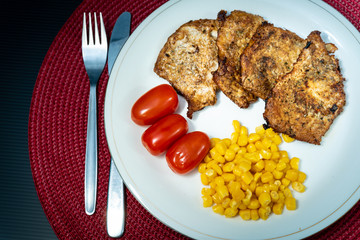 Roast meat, three cherry tomatoes and some sweet corn on a plate