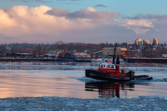 New Westminster, Vancouver, BC, Canada - January 16, 2020: Industrial Tugboat pulling a load in Fraser River during a colorful winter sunset with ice in the water.
