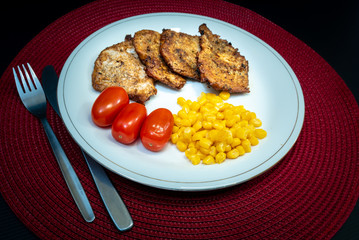 Roast meat, three cherry tomatoes and some sweet corn on a plate