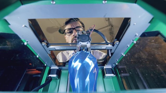 A man is watching a blue vase getting 3D-printed