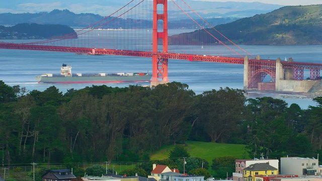 Aerial view of the magnificent Golden Gate Bridge with a cargo ship passing under it. This bridge connects the San Francisco peninsula to Marin County. US route 101 and SR 1 full of cars. Red 8K.