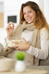 smiling woman eating pop corn on the sofa