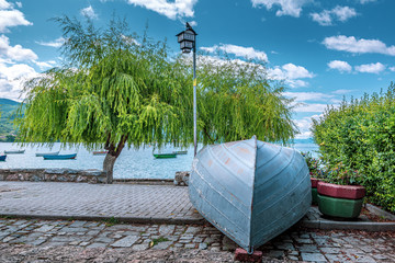 Close up of one boat on the beach and one three in the background. Ohrid Lake, Spring,  North Macedonia. - obrazy, fototapety, plakaty