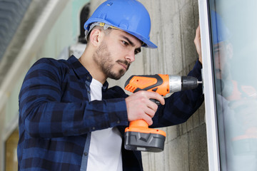 handyman using a cordless screwdriver to install a window