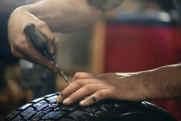 Worker of auto service seals with a tourniquet of a punctured car wheel close up. Defocused photo.