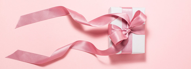 Banner of white gift box with a purple satin ribbon bow on pink flat lay