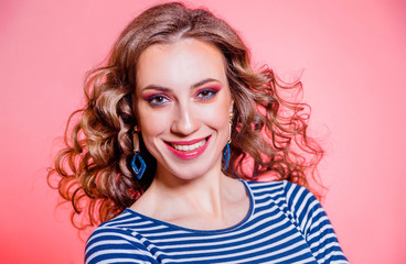 Happy beautiful brunette girl with red makeup, curly hair and a blue stripes sweater posing against a red background