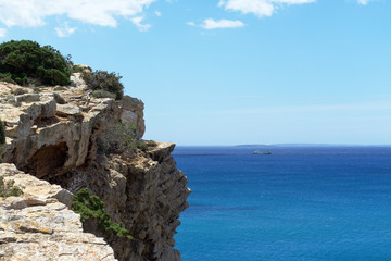 Fototapeta na wymiar Rocky sea coast with clean blue water, cloudy sky and city view. Ibiza island, Spain