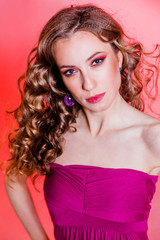 Sensual beautiful brunette girl with red makeup, curly hair and a burgundy top posing on a red background