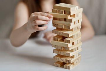 Little girl plays jenga in white clothes on a light background