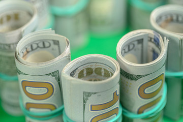 hundred-dollar bills in rolls on a green background