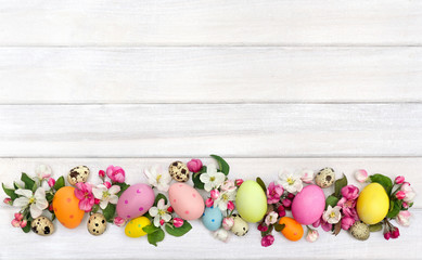 Obraz na płótnie Canvas Easter decoration. Pink flowers apple tree and colored easter eggs and quail eggs on background of white painted wooden planks with space for text. Top view, flat lay