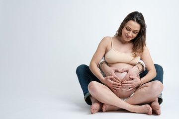 Young man holding belly of his pregnant wife making heart. Pregnant woman and loving husband hugging tummy at home. Heart of hands by lovely couple on pregnant belly. Copyspace, isolated