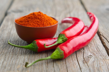 Whole and ground to powder red chili pepper on wooden kitchen table.