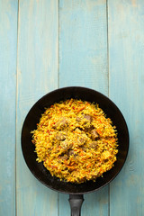 Dish of oriental cuisine - pilaf with lamb in a pan, on a wooden background.