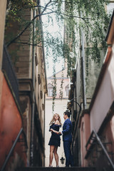 Obraz na płótnie Canvas Stylish couple embracing together in european city street on background of old architecture. Fashionable man and woman in love enjoying day in city. Traveling together in Europe