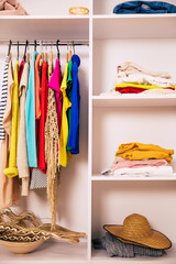 Well-organized space. Close-up shot of a part of a compartment wardrobe full of clothes, which is hanging in it and laying on several shelves.