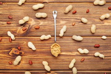 Vintage spoon with creamy peanut butter on a brown wooden table. Near the peanut butter lies peanuts in the shell and peeled peanuts. Flat lay of peanut paste for cooking breakfast.Vegan food concept