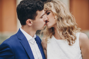 Stylish couple embracing and kissing in european city street. Sensual passionate moment. Fashionable bride and groom in love gently hugging. Valentines day