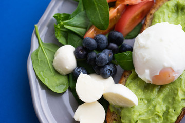 Wholesome tasty full of vitamins and health breakfast with avocado, berries, cheese and tomatoes with basil.