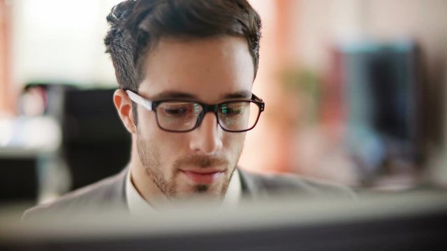 Handsome young man working in a touchscreen computer or tablet. Businessman with glasses in an office space. Technology. Daylight. Dolly shot. 