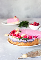 Piece of raspberry cream mousse cake (no baked cheesecake) decorated with fresh raspberries, mini cookies and coconut flakes on light grey background.