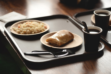 Stuffed pancake, pilaf and a hot tea in a paper cup on the cafe table background.