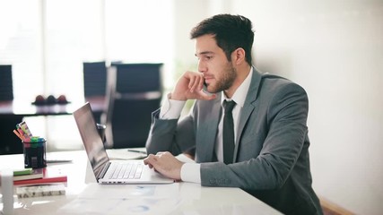 Handsome and young businessman using smartphone in the office. He is talking on the phone, laughing and working on a laptop. Dolly shot. Daylight. Technology.  - Powered by Adobe